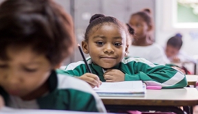 Smiling girl & other children working at their desks in elementary school